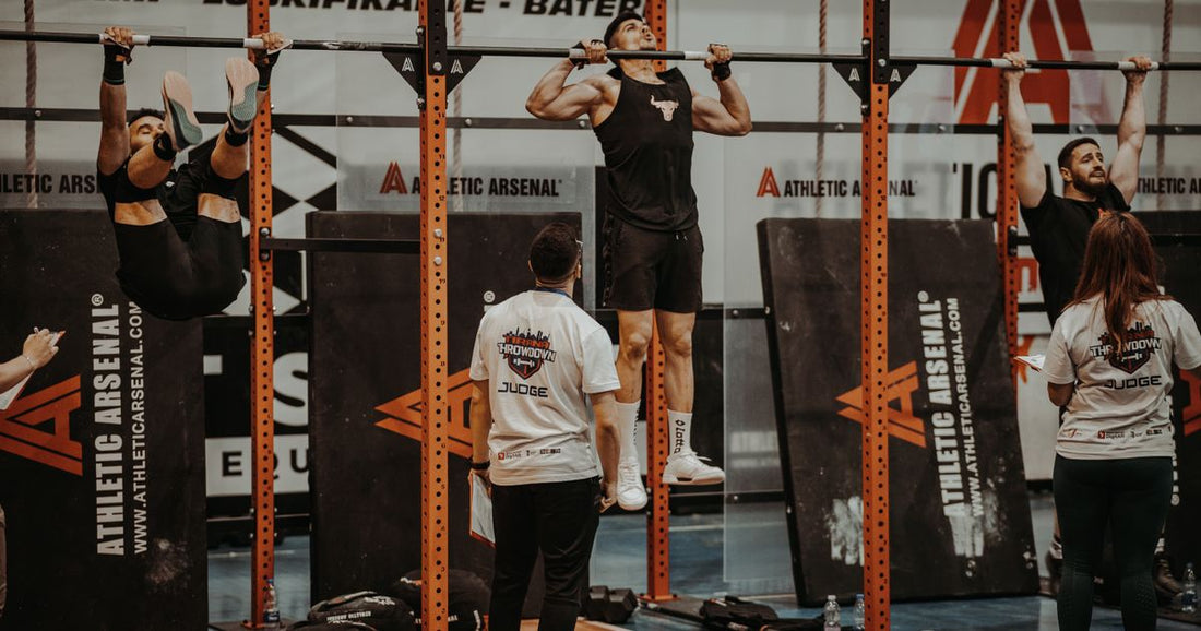 Athletes competing on pull-up bars in a gym, with one athlete raising toes toward the bar