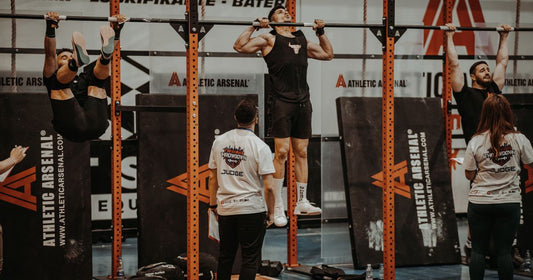 Athletes competing on pull-up bars in a gym, with one athlete raising toes toward the bar
