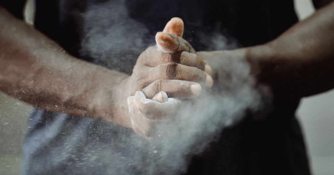Close-up of an athlete clapping powder chalk between their hands, with a cloud of chalk dust in the air