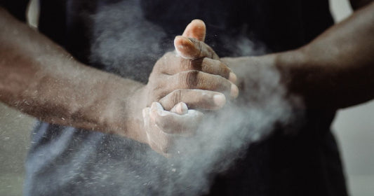 Close-up of an athlete clapping powder chalk between their hands, with a cloud of chalk dust in the air