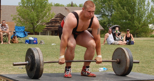 Lifter crouched in his deadlift setup, gripping a loaded barbell on an outdoor platform.